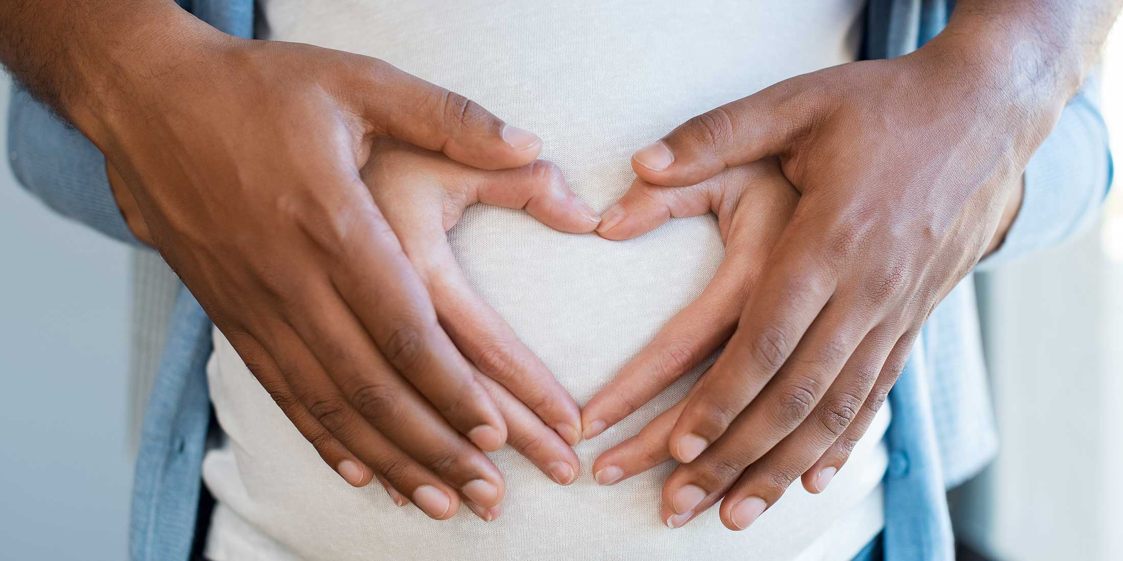 Couple with their hands in the shape of a heart on pregnant woman's belly