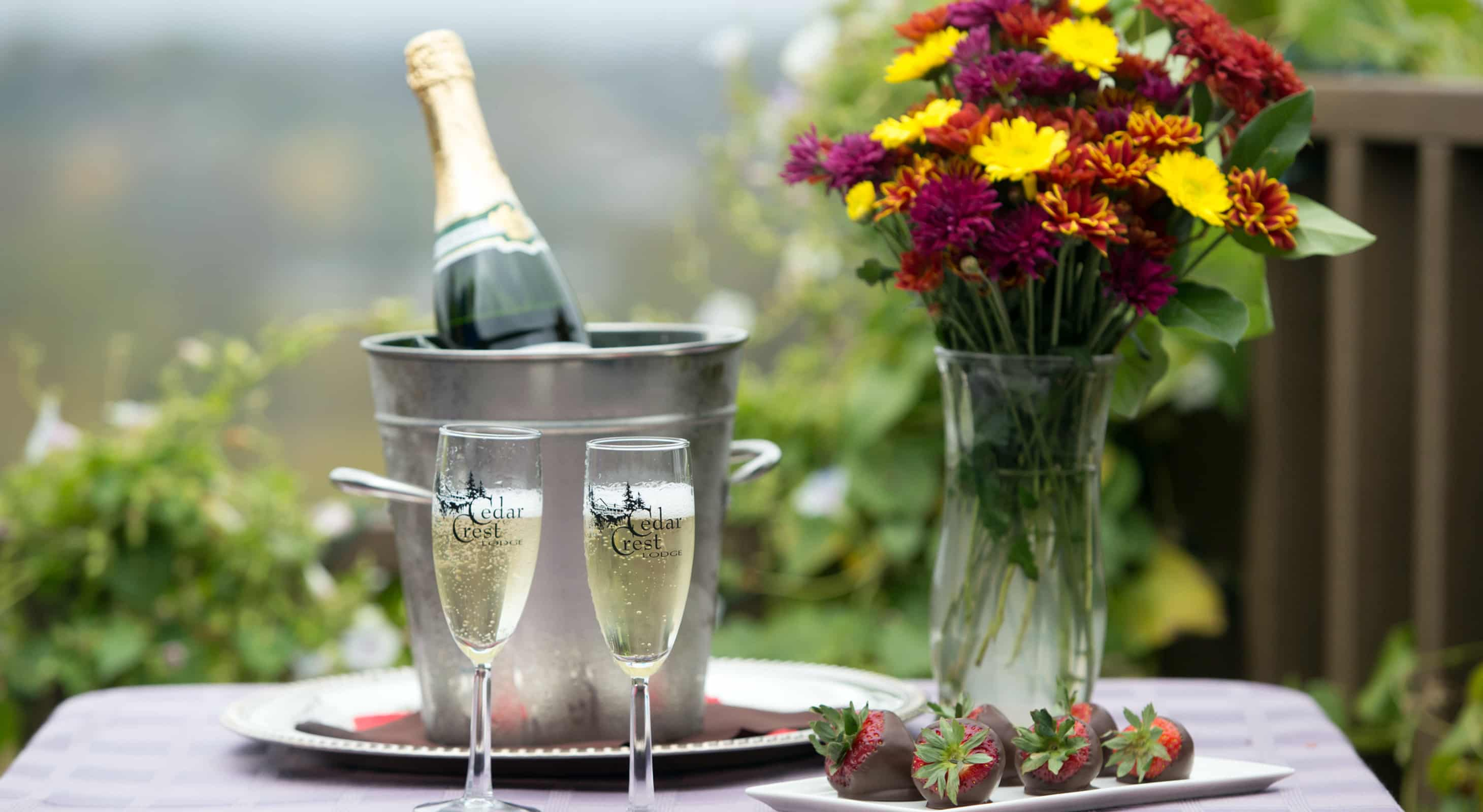 Champagne, chocolate-covered strawberries & flowers on a table outside