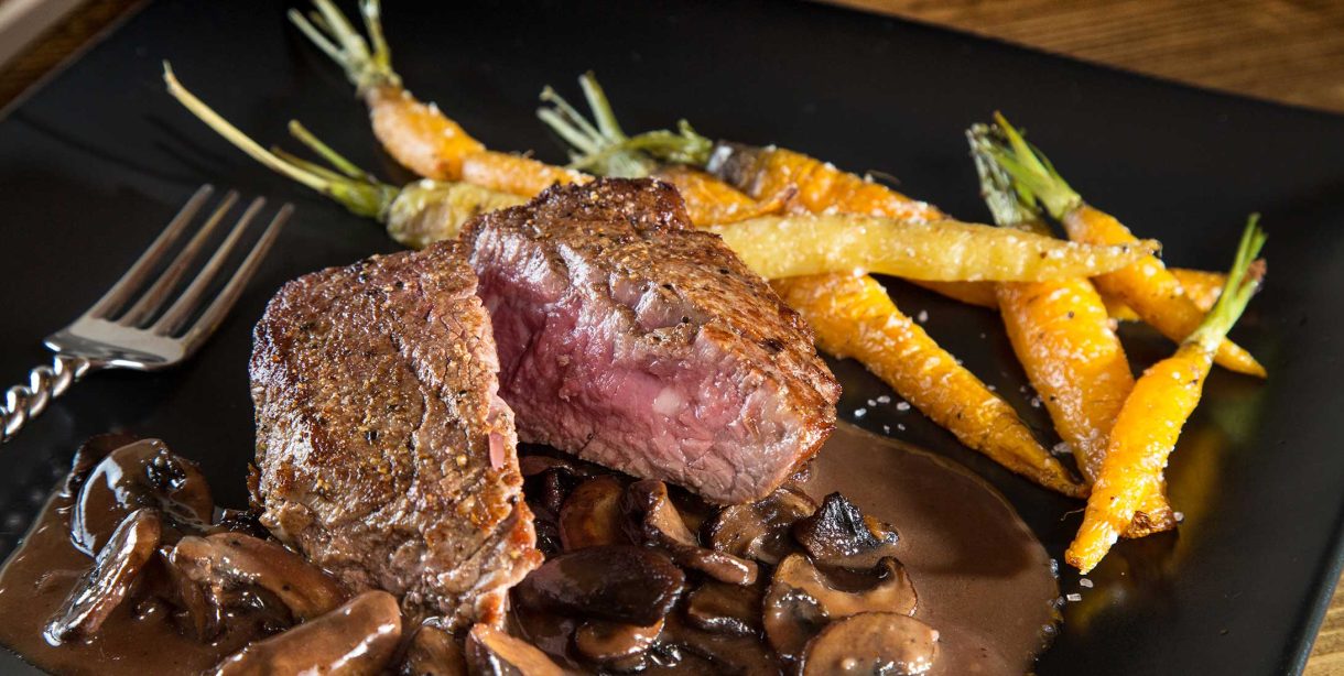 Dinner of steak and roasted carrots on a dark plate
