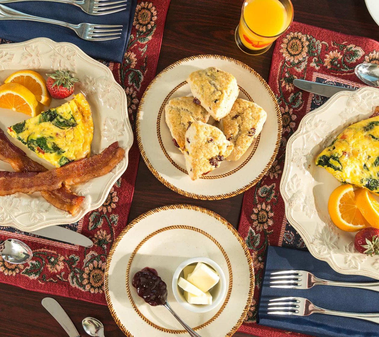 spread of breakfast foods on table with quiche, eggs, bacon, and fresh fruits