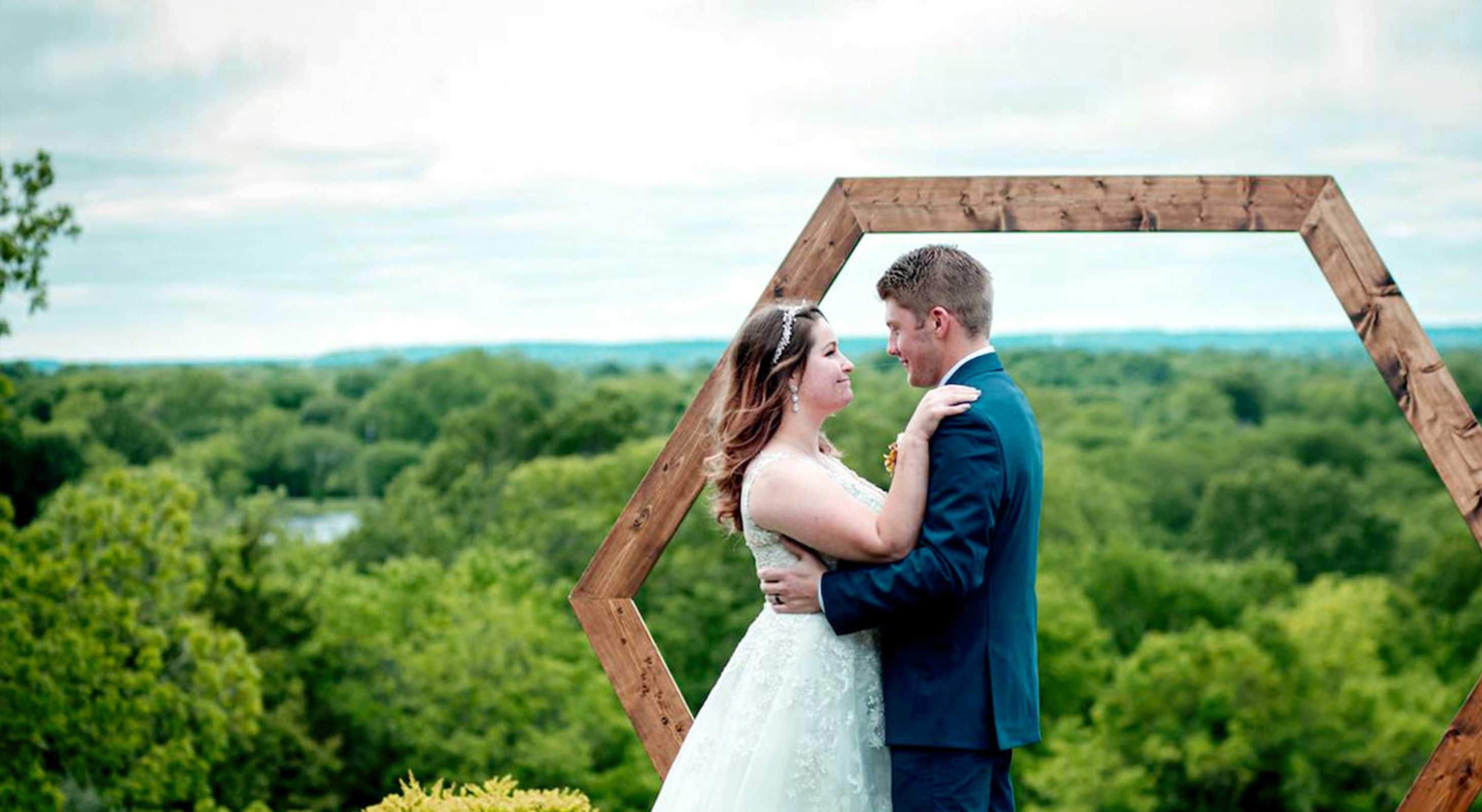 Bride and groom in front of a wooden arch and beautiful views at Kansas wedding venue