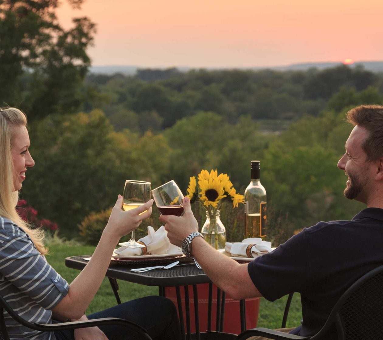Couple toasting glasses of wine on the patio at sunset