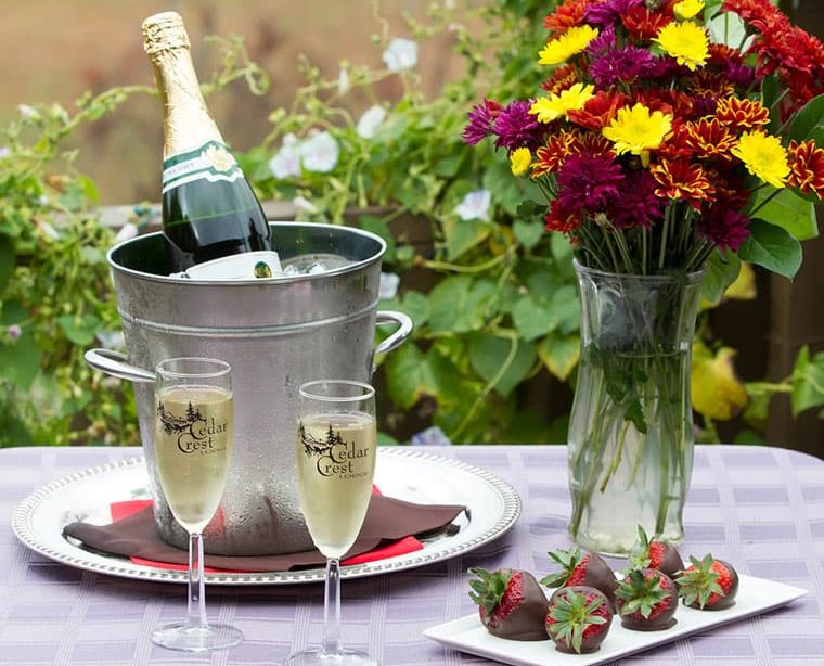 Bottle of champagne with two flutes and nearby plate of chocolate strawberries