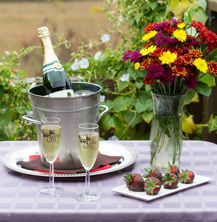 Bottle of champagne with two flutes and nearby plate of chocolate strawberries
