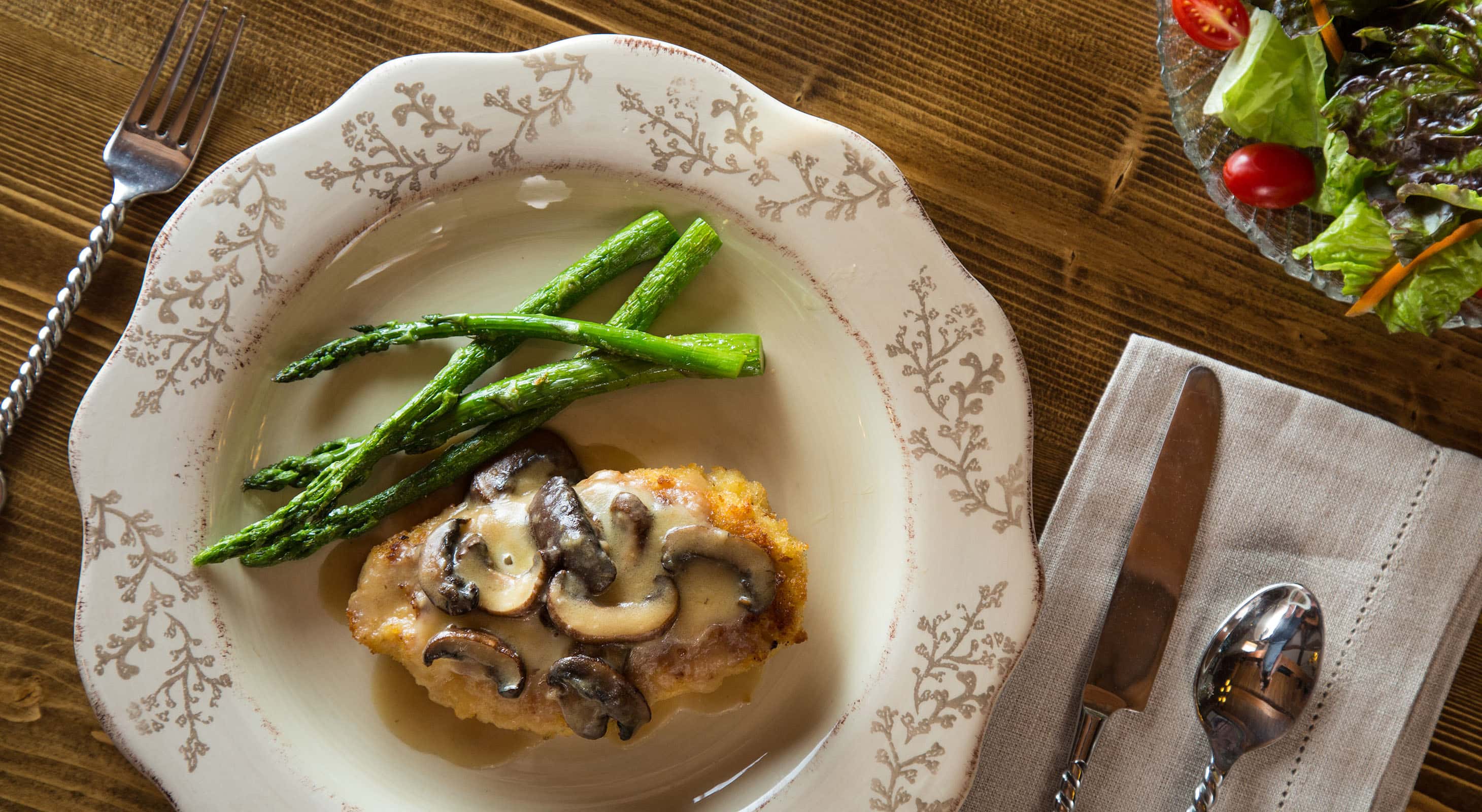 Dish with chicken, mushrooms, and asparagus alongside side salad