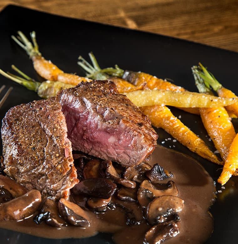 Cast iron plate with steak cuts and fresh carrots