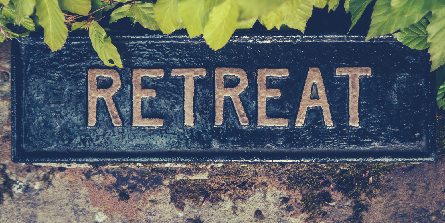 metal sign reading retreat surrounded by green leaves 