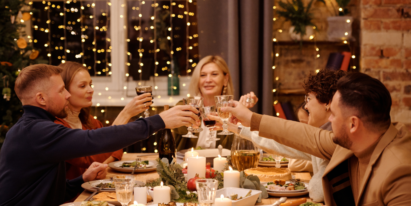 group of people raising glasses in a toast at a festive holiday dinner with candles and lights