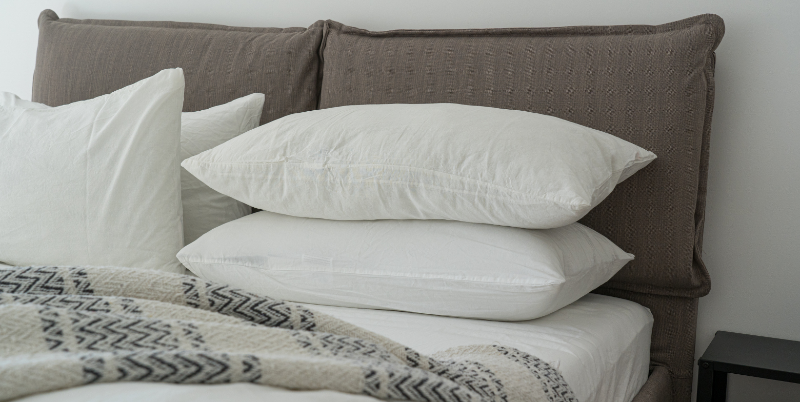 white pillows stacked on a neatly made bed with a patterned blanket and cushioned headboard
