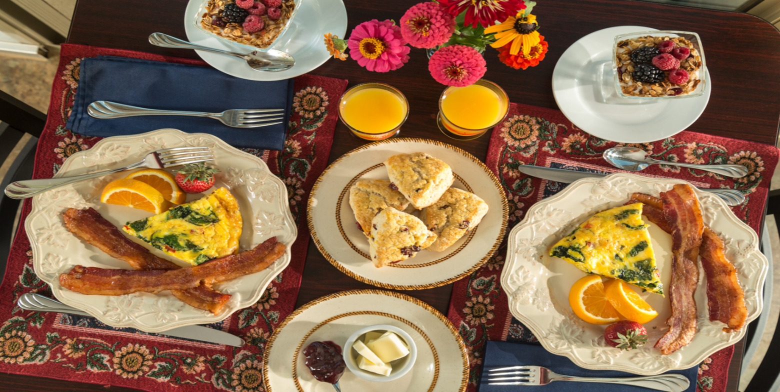 Gourmet breakfast at Cedar Crest Lodge featuring bacon, egg frittata, fresh fruit, scones, and orange juice.